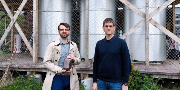 ETH researchers Samuel Heiniger (left, with a glass of iron ore) and Professor Wendelin Stark in front of the three iron reactors on the Hönggerberg campus of ETH Zurich. 